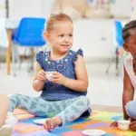 Little girls having a tea party while playing on a colourful mat on the floor at preschool or kinde.