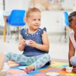 Little girls having a tea party while playing on a colourful mat on the floor at preschool or kinde.