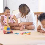On a holiday, A mother and her two little daughters sit on the floor and drawing together in the living room